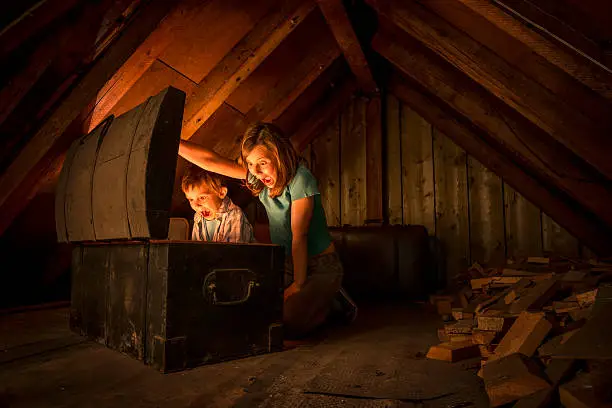 two surprised kids opening a glowing treasure chest at the attic of an old house