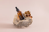 Cosmetic bottle with a dropper with a natural product for the care of aging skin of the face on a large gray textured stone with a dried flower