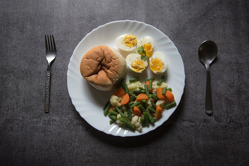 View from above of healthy breakfast food bread, eggs and boiled vegetables on a plate. Selective focus.