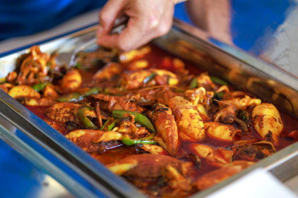 A cropped image capturing a man using a spoon to carefully select his food from the buffet line.