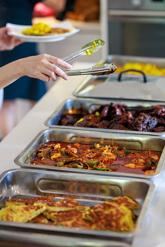 A cropped image captures people using service tongs to carefully select their food from the buffet line