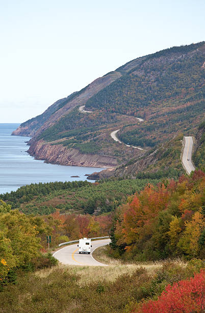 RV on a Scenic Highway Along The Sea "An RV crusing along a highway through a colourful forest along the sea. Cabot Trail. Nova Scotia, Cape Breton, Canada. Fall scenic. Vertical colour image." cabot trail stock pictures, royalty-free photos & images