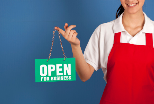 Female small business owner holding up OPEN FOR BUSINESS sign