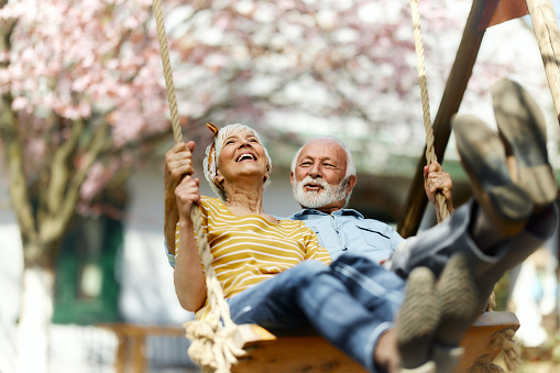 Happy senior couple having fun while swinging during spring day in the park.