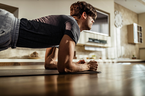 Determined athletic man exercising in plank position on a floor in the living room. Copy space.