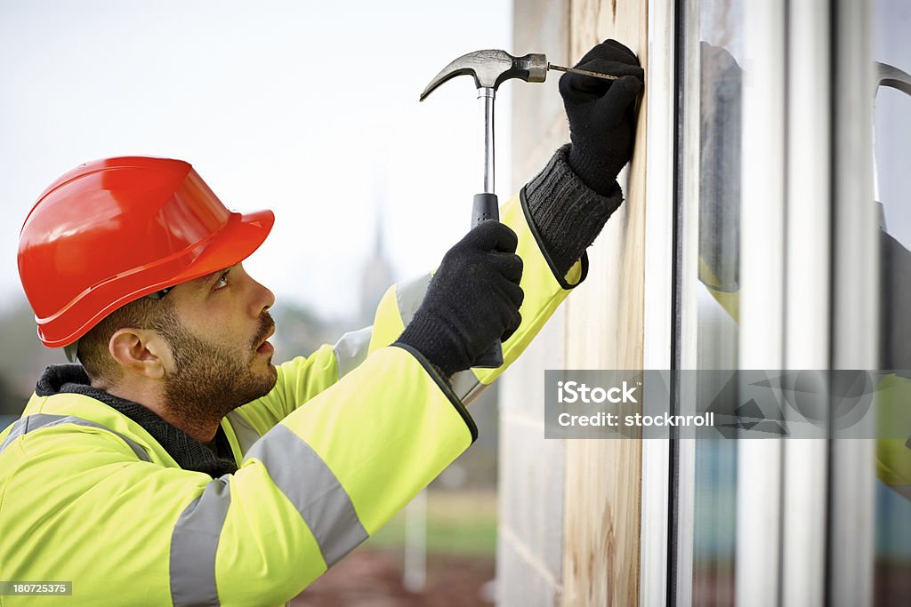 Construcción trabajador utiliza un martillo para recorrer clavos en pared - Foto de stock de 25-29 años libre de derechos