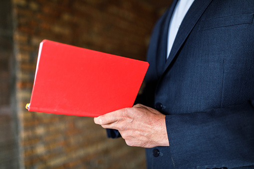 Close up of unrecognizable businessman reading plans from a red notebook. Copy space.