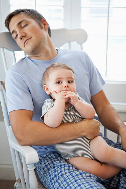 Father napping with baby in lap Tired young father (20s) resting in rocking chair with baby (8 months) sitting on lap.  Focus on baby. Sc0601 stock pictures, royalty-free photos & images