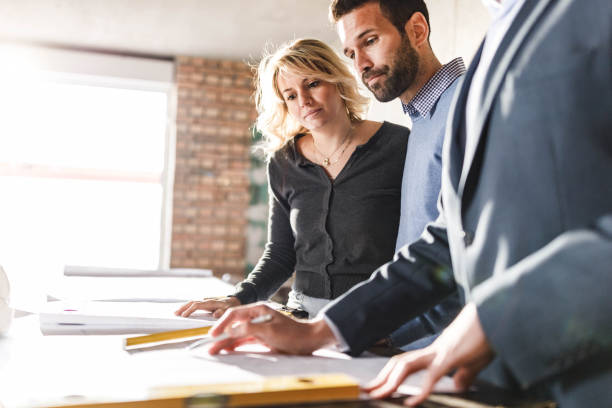 istock Young couple and male architect analyzing blueprints at construction site. 1807259090