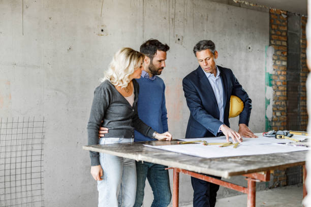 istock Young couple and their architect examining blueprints at construction site. 1807259639