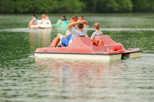Girl and boy using pedal boat on lake with other recreation activities in background.