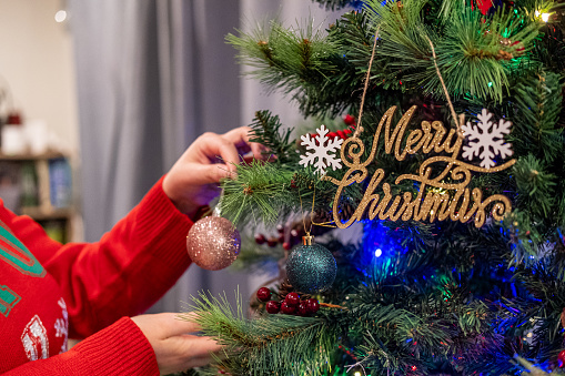 A human hand places glitter ball christmas decoration onto christmas tree