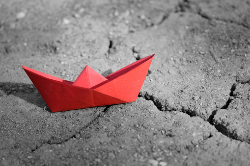 Red paper ship on cracked overdried soil