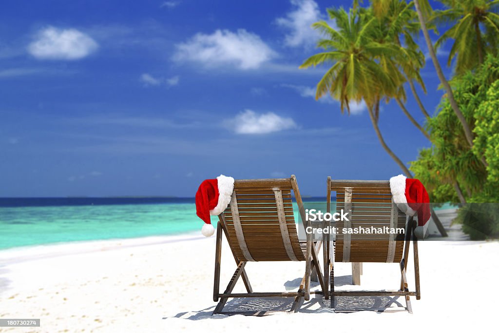 Christmas card Christmas card or background - two sunloungers with Santa hats standing on beautiful tropical beach with palm trees, white sand and turquoise water on Maldives. Concept of perfect vacation. Christmas Stock Photo