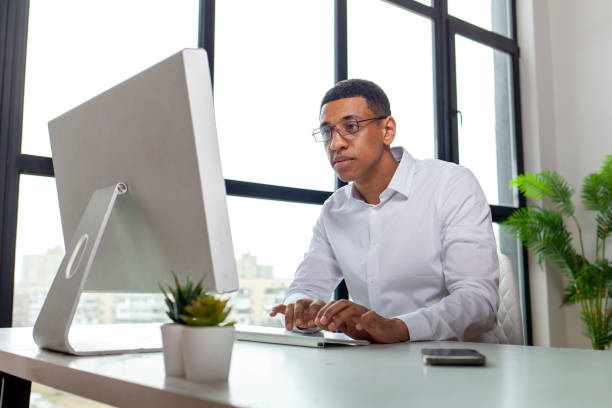 istock African American office worker in glasses and shirt sits at table and types on computer, businessman works online 1807312993
