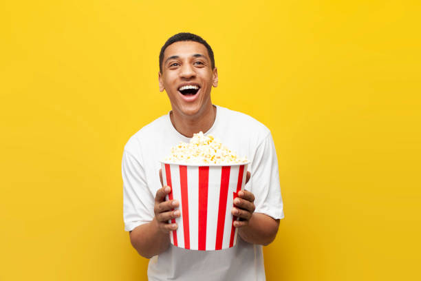 istock young african american guy with popcorn watching comedy and laughing on yellow isolated background, cinema viewer 1807316548