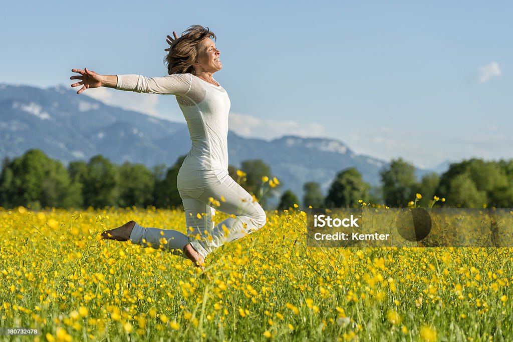 happy mature woman jumping in flower meadow smiling mature woman jumping barefoot in flower meadow with arms outstretched Women Stock Photo