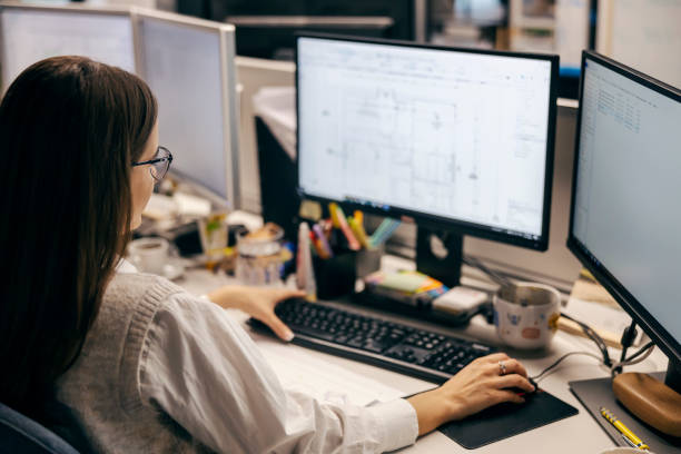istock Rear view of a female architect working on blueprints at the office. 1807329409