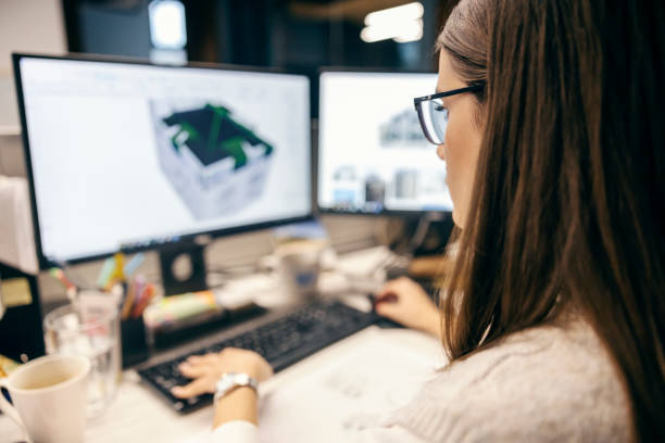 istock Rear view of an architect working on a computer and drawing blueprints. 1807331009