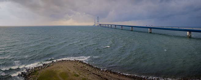 View from the coast of Denmark, one can see the Storebælt Bridge spanning across the horizon, connecting the two coasts. Scenic transportation network on the Great Belt Bridge.