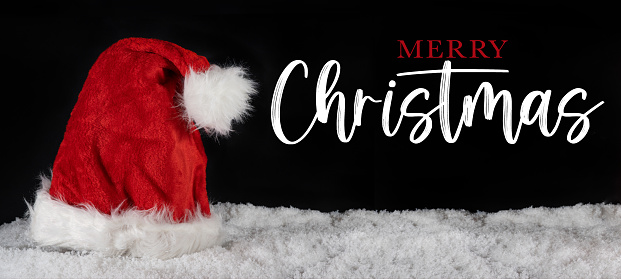 Merry Christmas celebration holiday banner greeting card with text - Santa Claus cap on snow, isolated on black background