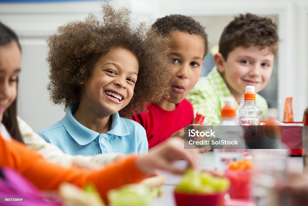 Young Students Enjoying Lunchtime Group of children sitting down at a table eating and enjoying their lunch at school Child Stock Photo