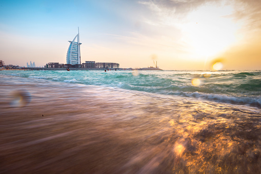 Dubai, United Arab Emirates, April 15, 2021: Kite Beach in Dubai, bustling with visitors, offers a stunning sunset backdrop, with the iconic Burj Al Arab hotel standing tall against the warm hues of a sunny day, captured through a longer exposure.