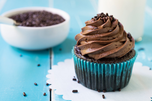 A chocolate cupcake on a blue table with a bowl of chocolate sprinkles.