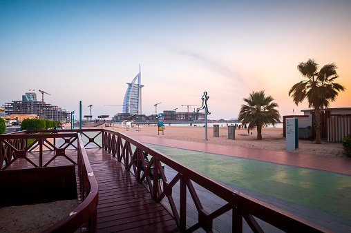 Dubai, United Arab Emirates, April 15, 2021: Kite Beach running and walking tracks in Dubai, bustling with visitors, offers a stunning sunset backdrop, with the iconic Burj Al Arab hotel standing tall against the warm hues of a sunny day