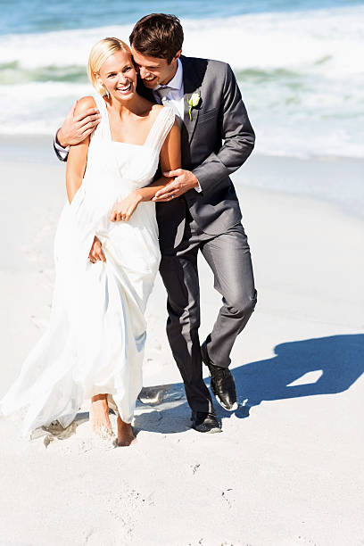 Full length of loving bride and groom walking on beach. Vertical shot.