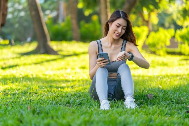 istock Asian Woman Utilizing Technology for Health, Analyzing Smartwatch Data During Leisure Exercise in a Public Park at Sunset. Asian Woman Using Technology For Health And Wellness. Empowering Wellness. 1807370557