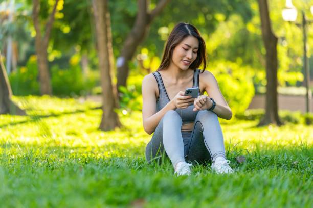 istock Asian Woman Utilizing Technology for Health, Analyzing Smartwatch Data During Leisure Exercise in a Public Park at Sunset. Asian Woman Using Technology For Health And Wellness. Empowering Wellness. 1807371625