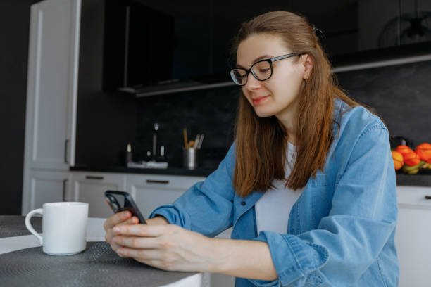 istock woman sitting in kitchen with smartphone, texting, browsing online services 1807372700