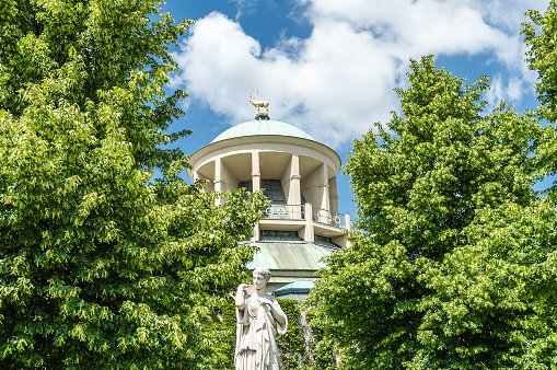 In the background you can see the representative dome with the golden deer, the emblem of Württemberg. The building is right next to the new castle on the northern flank of the castle square of Stuttgart, Germany. Some trees and a old statue in the front. Copy space on the sky.