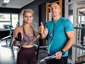 Male fitness trainer and female client showing thumbs up at gym