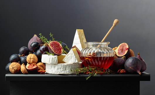 Camembert cheese with figs, grapes, walnuts, honey, and thyme. Soft cheese with fruits on a black background.