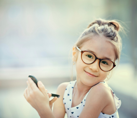 Little girl in glasses holding a mirror, smiling at camera