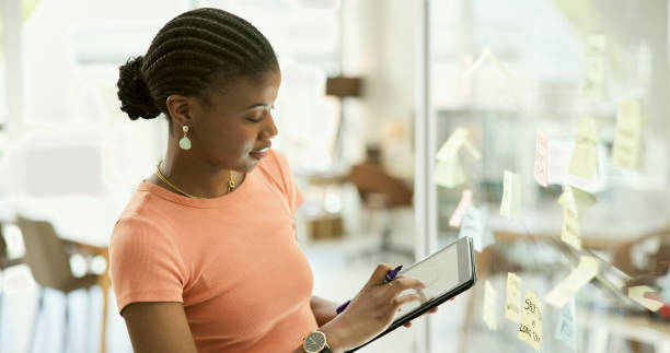 istock Black woman, tablet and schedule planning for ideas or creative strategy on glass board at office. African female person with technology for brainstorming, tasks or agenda in startup at workplace 1807417346