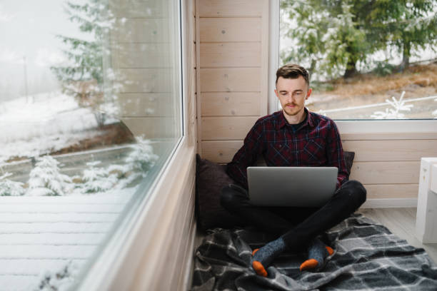istock Male working on laptop in front of panoramic window with great view of mountains. Remote work from cozy place. Workplace in house in snowy morning. Wide interior view. Concept freelance lifestyle 1807427953