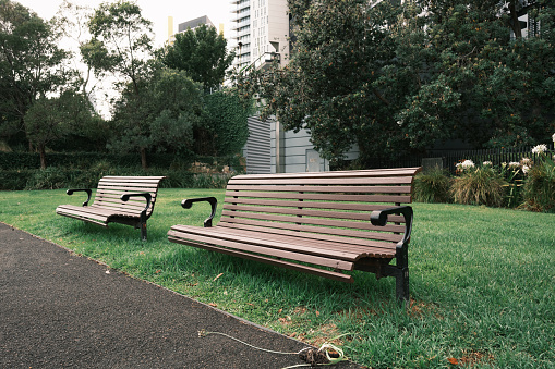 Two park benches on a patch of grass along a asphalt path.