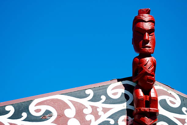 Marae Carving  & Sky A close-up of a Pou carving on the apex of the roof of a Marae against a clear blue summer's sky  motueka photos stock pictures, royalty-free photos & images