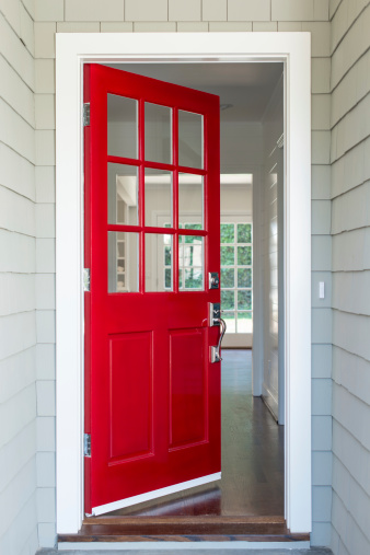 Front entrance to a residential home with a red solid wood door. The surrounding walls are covered with shingles.