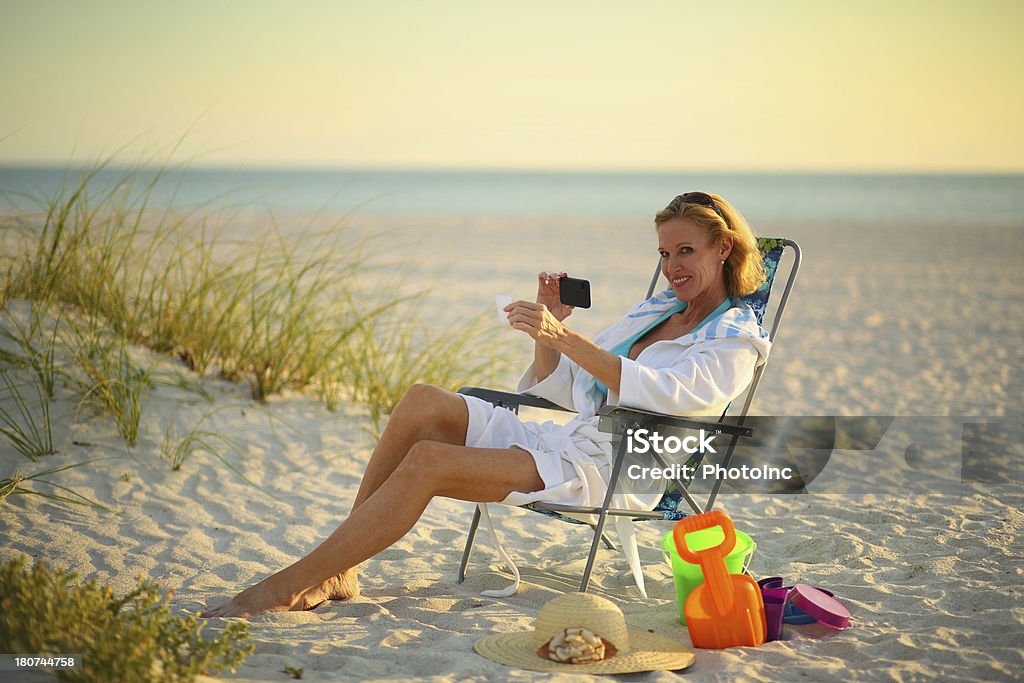 Mature Woman depositing check with mobile phone Mature Woman depositing check with mobile phone while sitting on the beach Beach Stock Photo