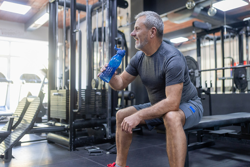 Elderly man maintains muscle strength in the gym, has a break