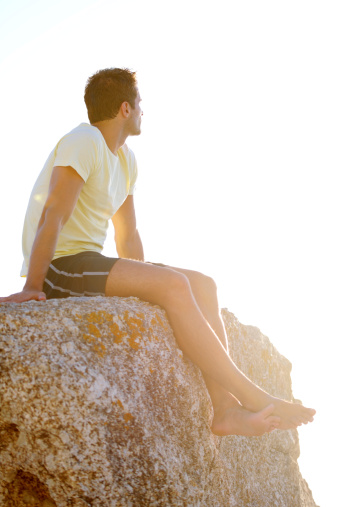Young man sitting on a rock with the sunset in the background