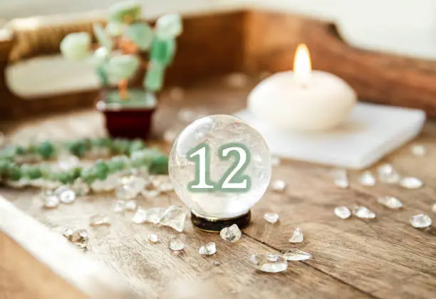 Number twelve on Gemstone sphere or crystal balls known as crystallum orbis and orbuculum. Natural clear quartz ball on stand on wood tray in home. Predictions concept.