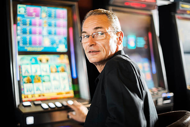 Mature man enjoys gambling in the casino on slot machines. He is looking at camera.