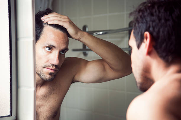 Checking Hairline Man checking hair in mirror. hair loss stock pictures, royalty-free photos & images