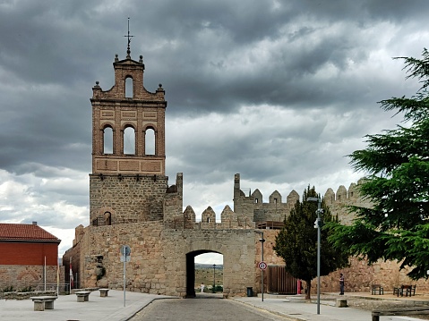Avila, Spain – May 04, 2023: Street going through the Carmen Gateway on the stone city wall and brick tower, in a sunny day at Avila. It has the longest and imposing wall complete