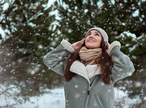 Happy young girl in a winter park looking at the snowfall.